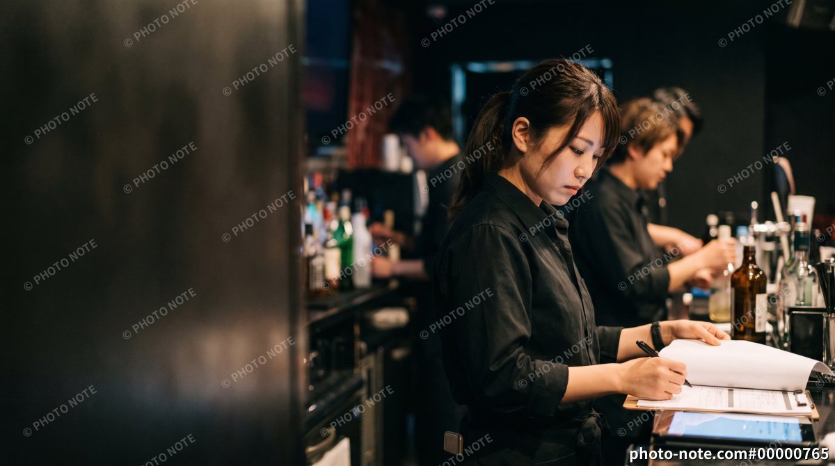 バーのカウンターで業務記録を記入する日本人女性スタッフ