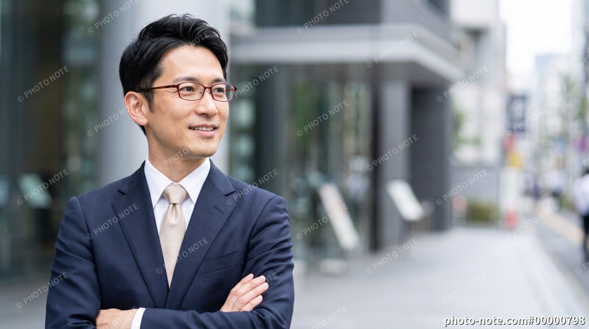 オフィス街で腕組みして微笑む男性ビジネスマン