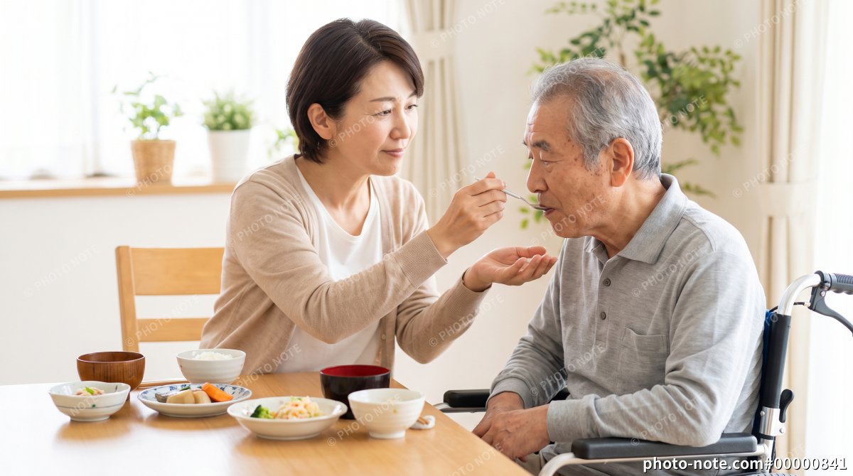自宅で車椅子の高齢男性の食事を介助する女性