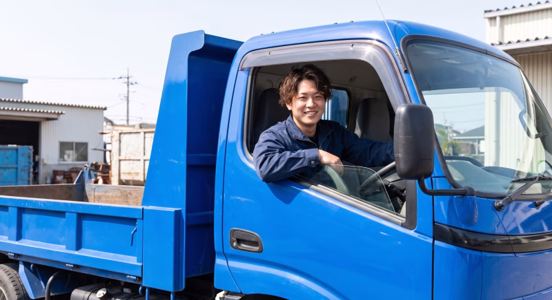 ダンプトラックの運転席で窓から顔を出す作業着の若い男性