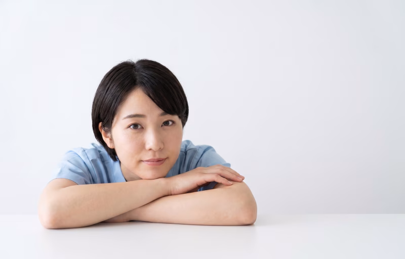 テーブルに腕を置いて正面を見つめる医療・介護スタッフの女性