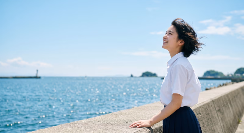 夏の海辺で青空を見上げる女子高校生