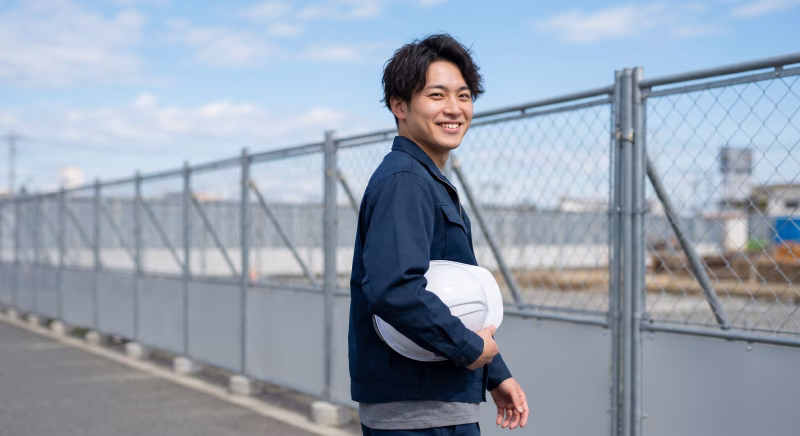 ヘルメットを持ち笑顔で振り返る男性作業員