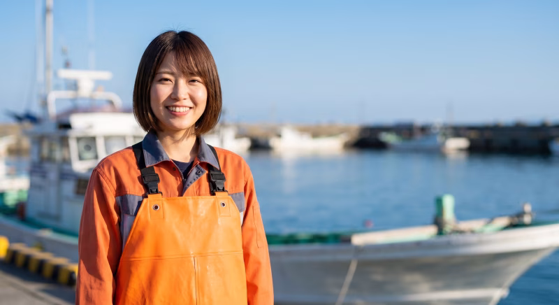 漁港で笑顔を見せる作業服姿の女性漁師