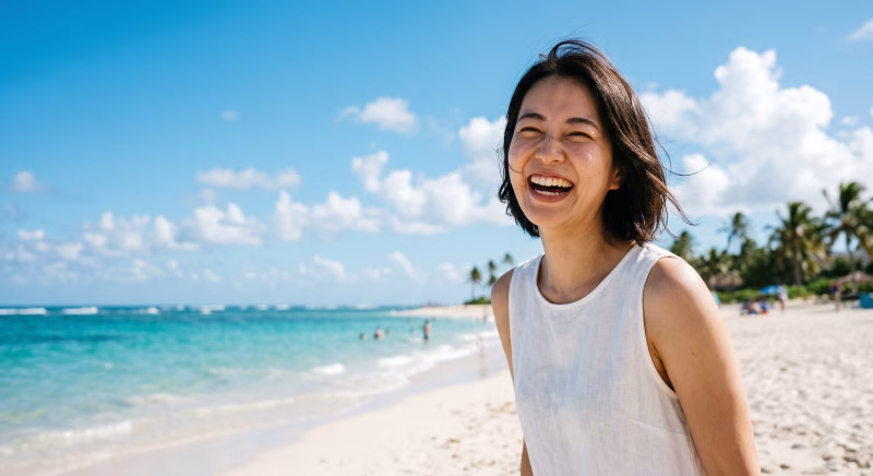 夏の海をバックに、砂浜で明るい表情を見せる女性
