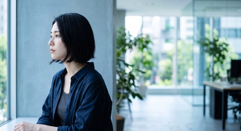 オフィスの窓辺で考え事をする若い女性
