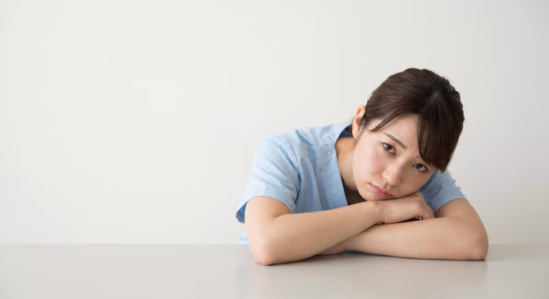 テーブルに腕を置いて疲れた表情を見せる医療スタッフの女性