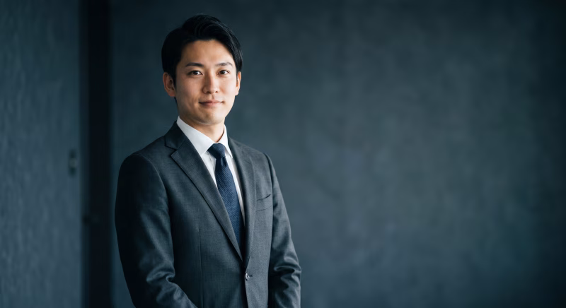 ダーク背景の前に立つ、自信に満ちた若手ビジネスマン