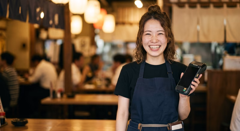 飲食店で決済端末を持つ笑顔の若い女性 、キャッシュレス決済