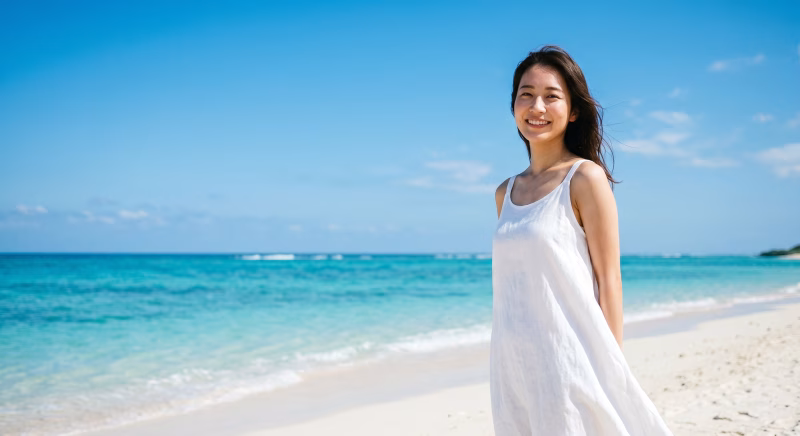 夏の海と砂浜をバックに、白いワンピースを着て佇む女性