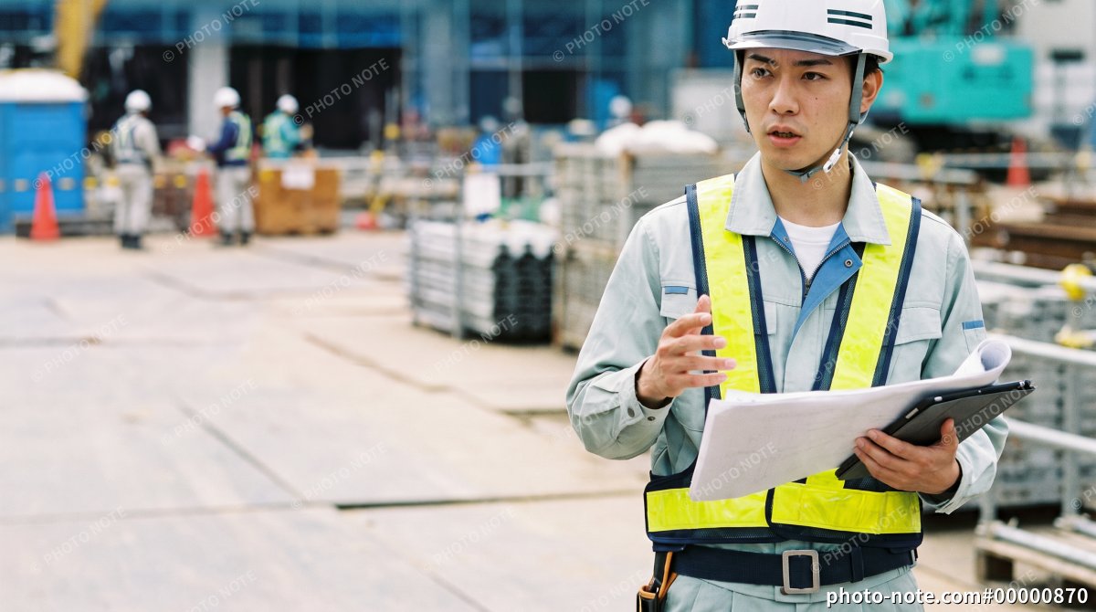 建設現場で図面とタブレットを確認しながら指示する施工管理の男性