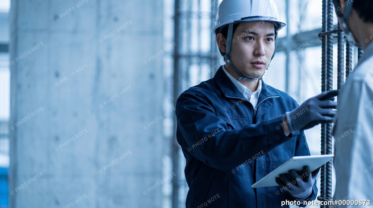 建設現場で鉄筋を確認しながら作業員と打ち合わせする施工管理の男性