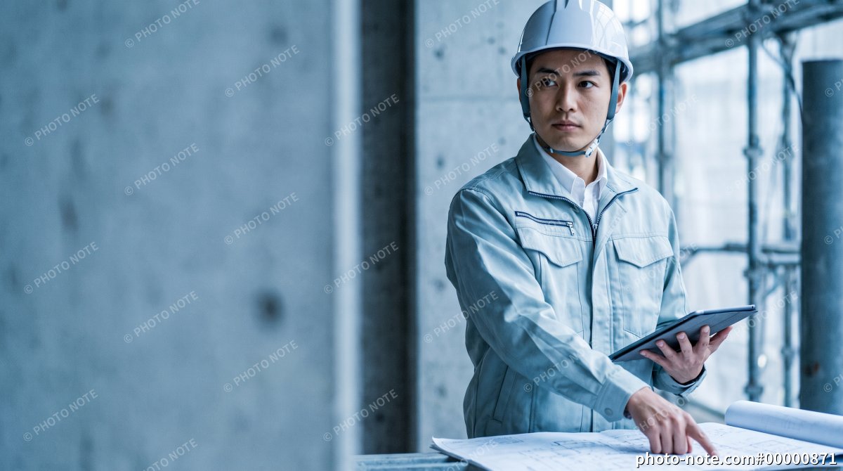 建設現場で設計図を確認しながら指示する施工管理の男性技術者