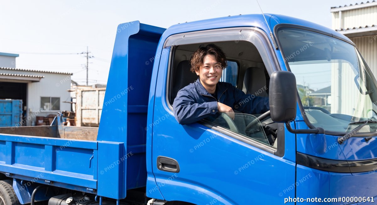ダンプトラックの運転席で窓から顔を出す作業着の若い男性
