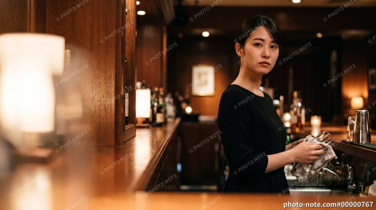 バーのカウンターでグラスを磨く日本人女性スタッフ
