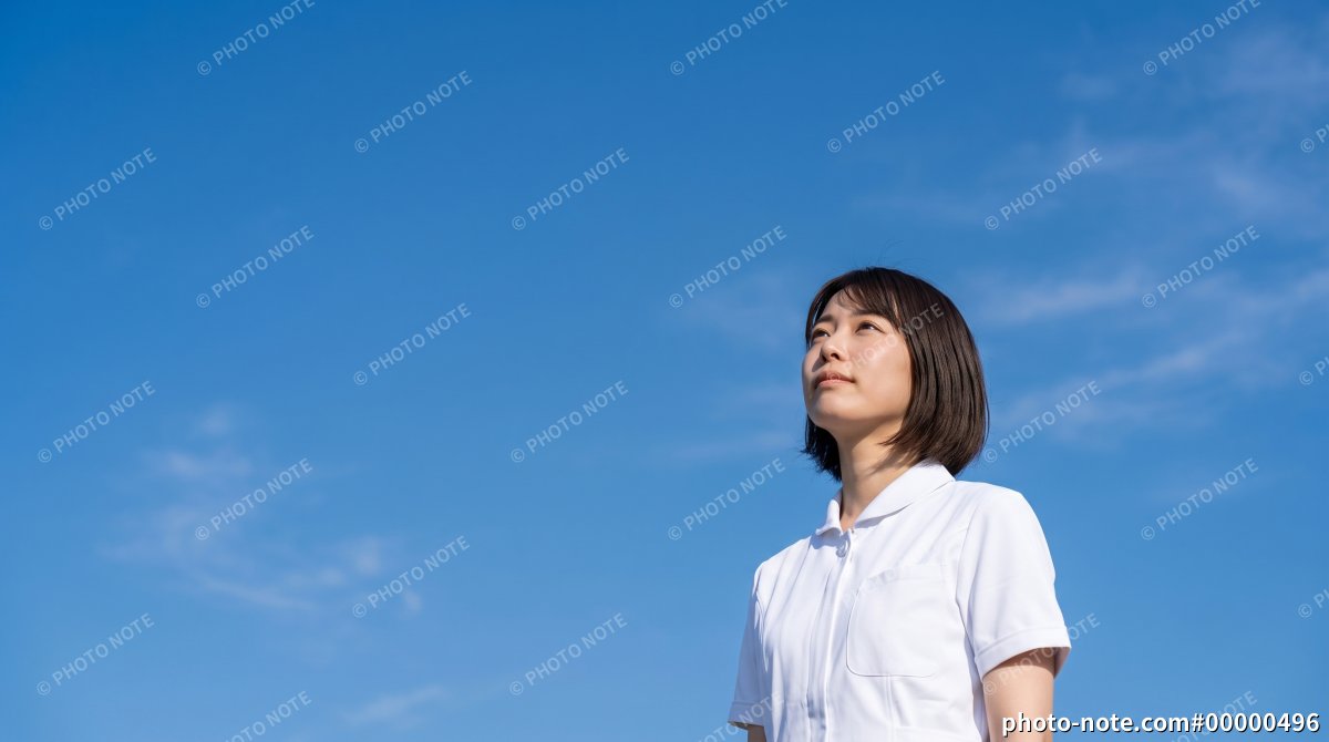 青空の下で遠くを見つめる白衣の看護師