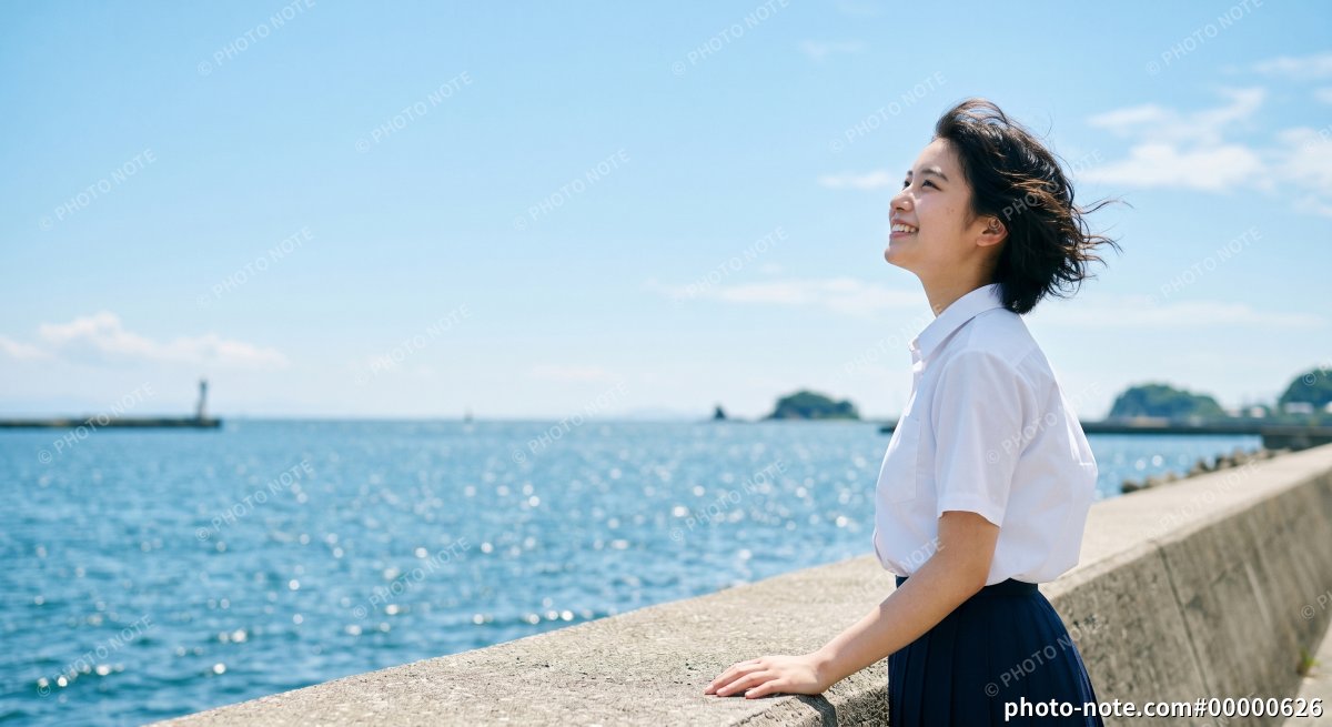 夏の海辺で青空を見上げる女子高校生