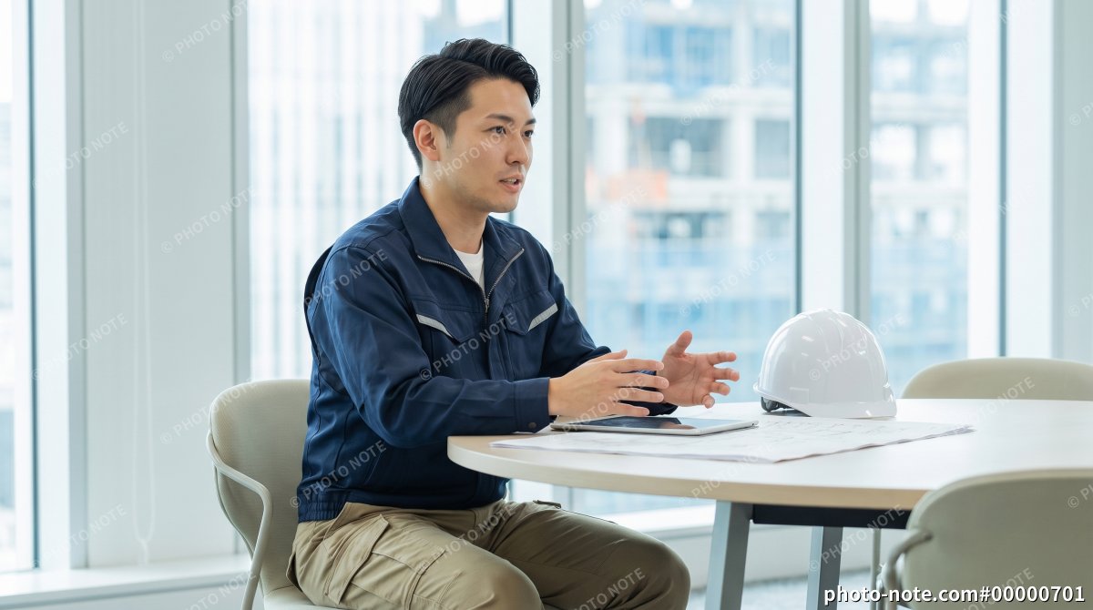 オフィスで図面を広げ打合せをする設計士や施工管理の男性
