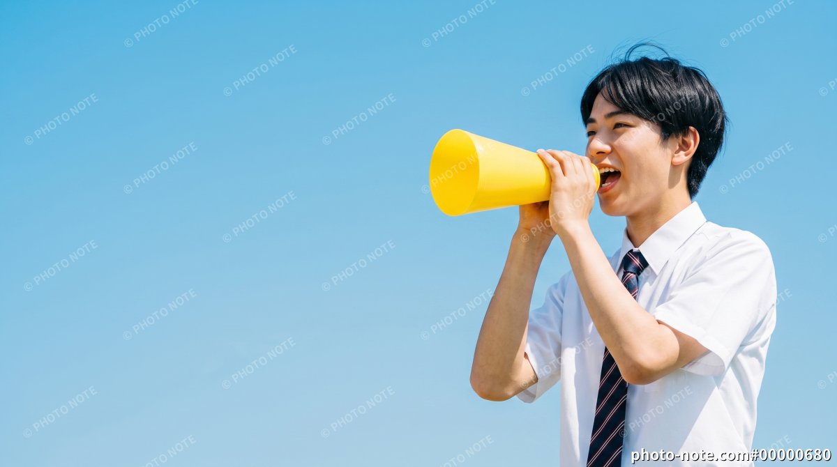青空を背景に黄色いメガホンを持って応援する夏服の男子学生