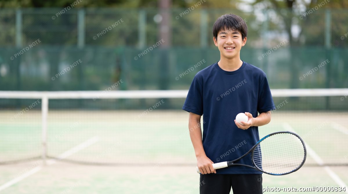 ソフトテニスのラケットとボールを持って笑顔を見せる男子学生