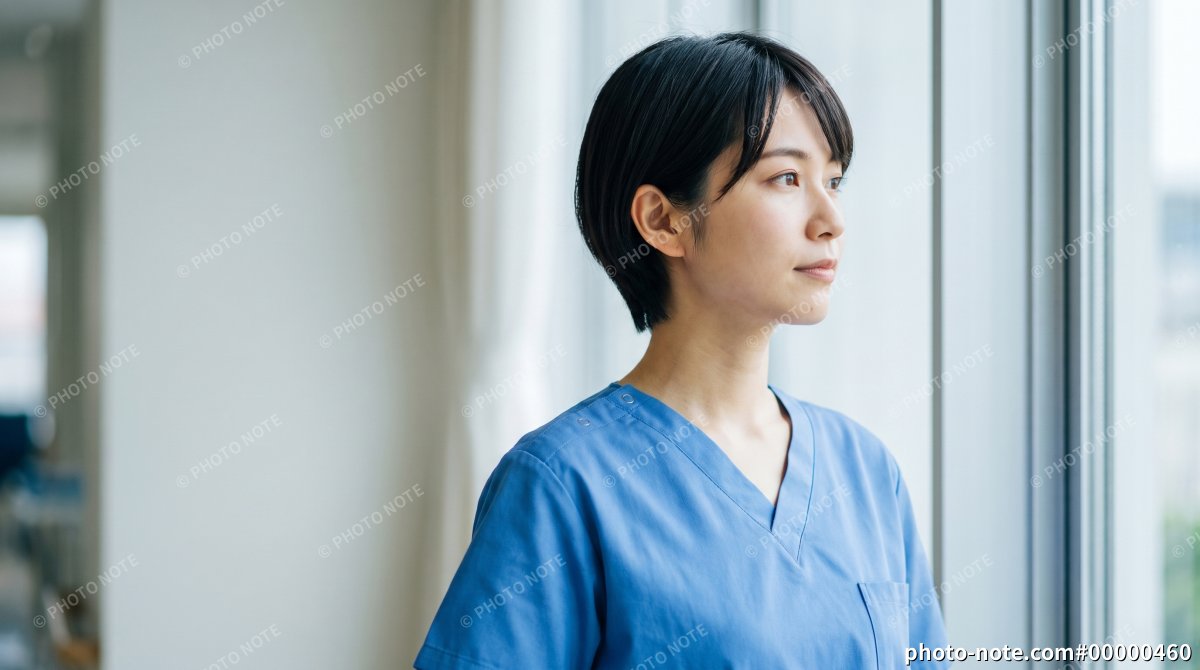 病院の窓際で外を見つめる看護師の女性