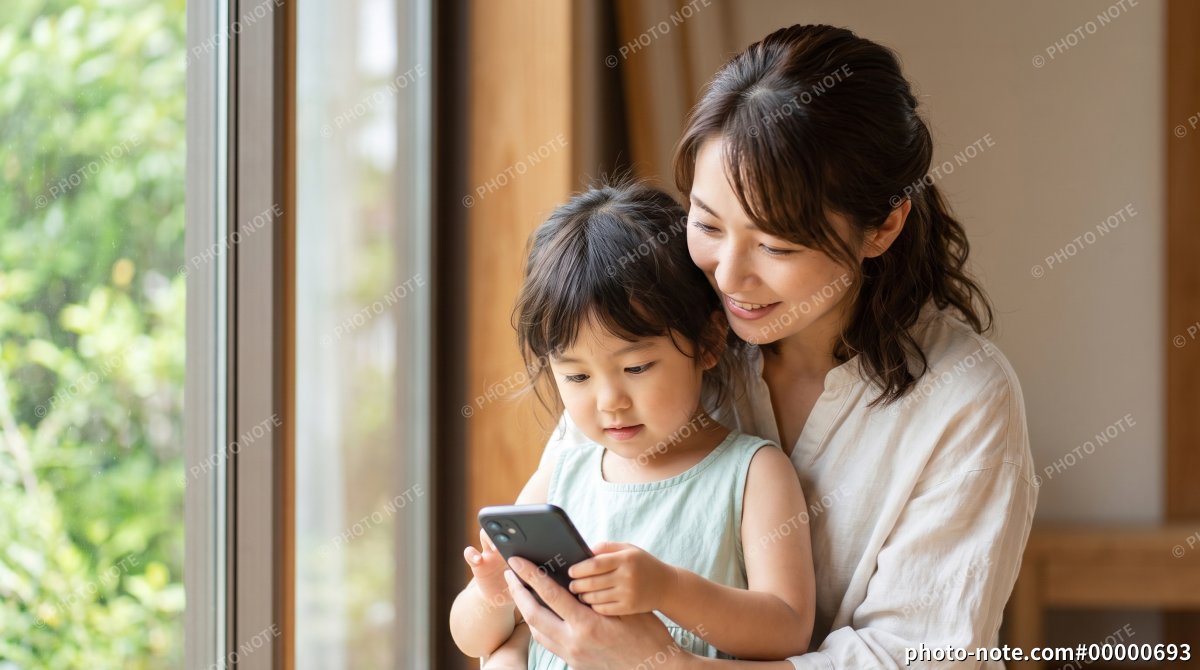 窓辺でスマートフォンを見る親子