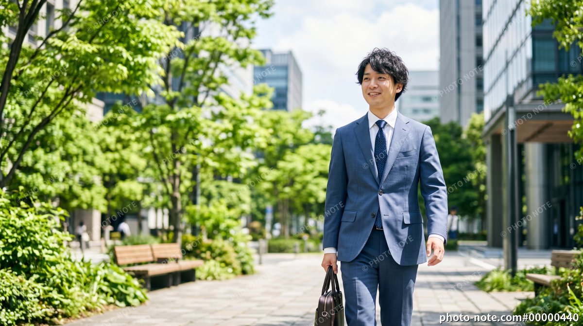 新緑のビジネス街を通勤する笑顔の20代男性会社員
