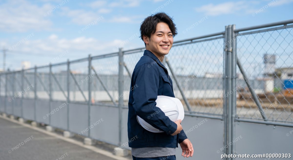 ヘルメットを持ち笑顔で振り返る男性作業員