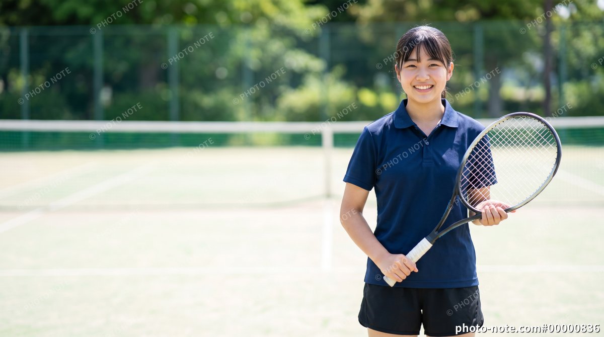 テニスコートでラケットを持って笑顔を見せる女子学生