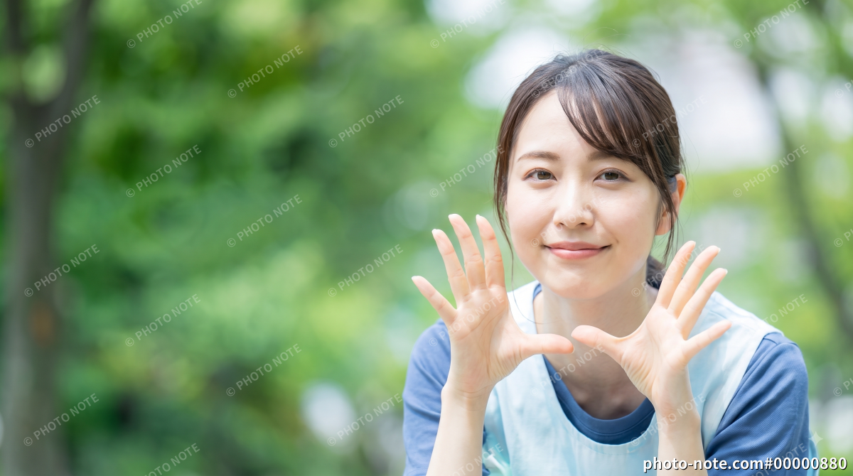 公園で両手を広げて笑顔で呼びかけるエプロン姿の保育士の女性