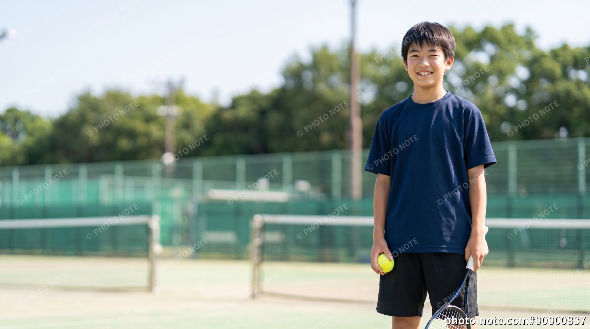 テニスコートでボールとラケットを持つ10代の男子学生