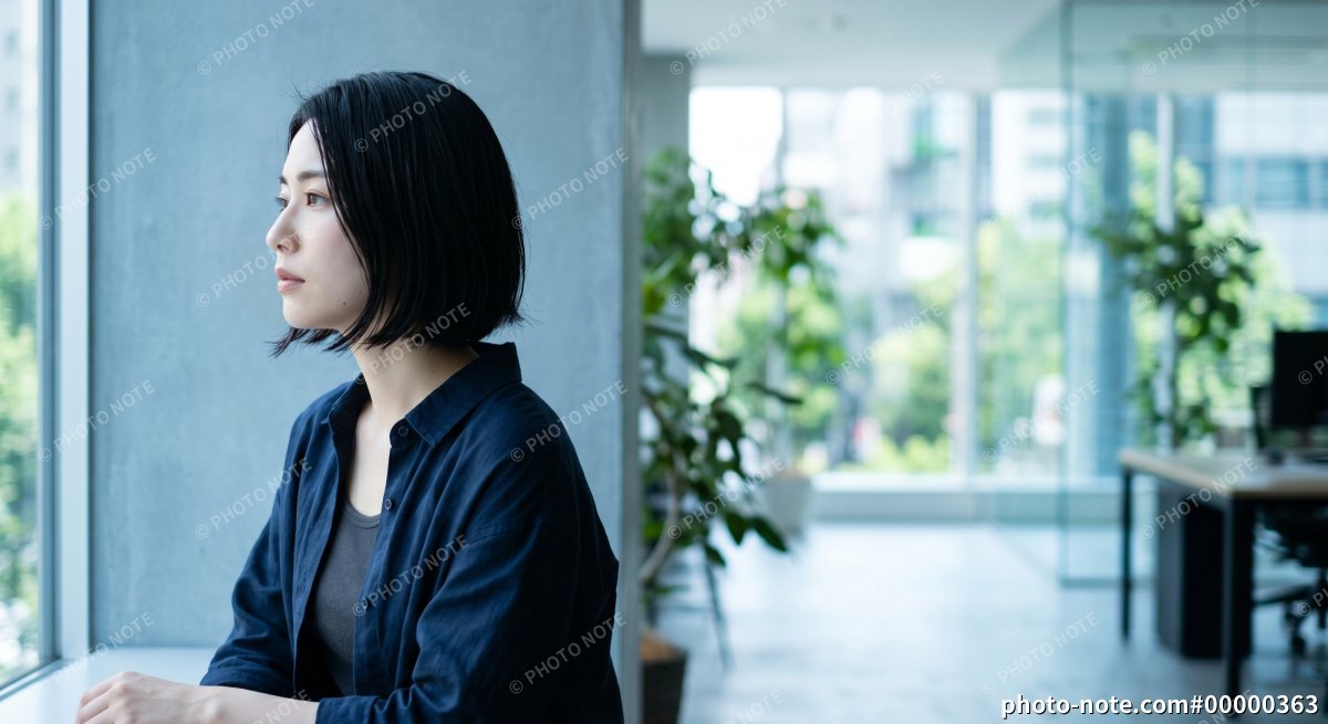 オフィスの窓辺で考え事をする若い女性