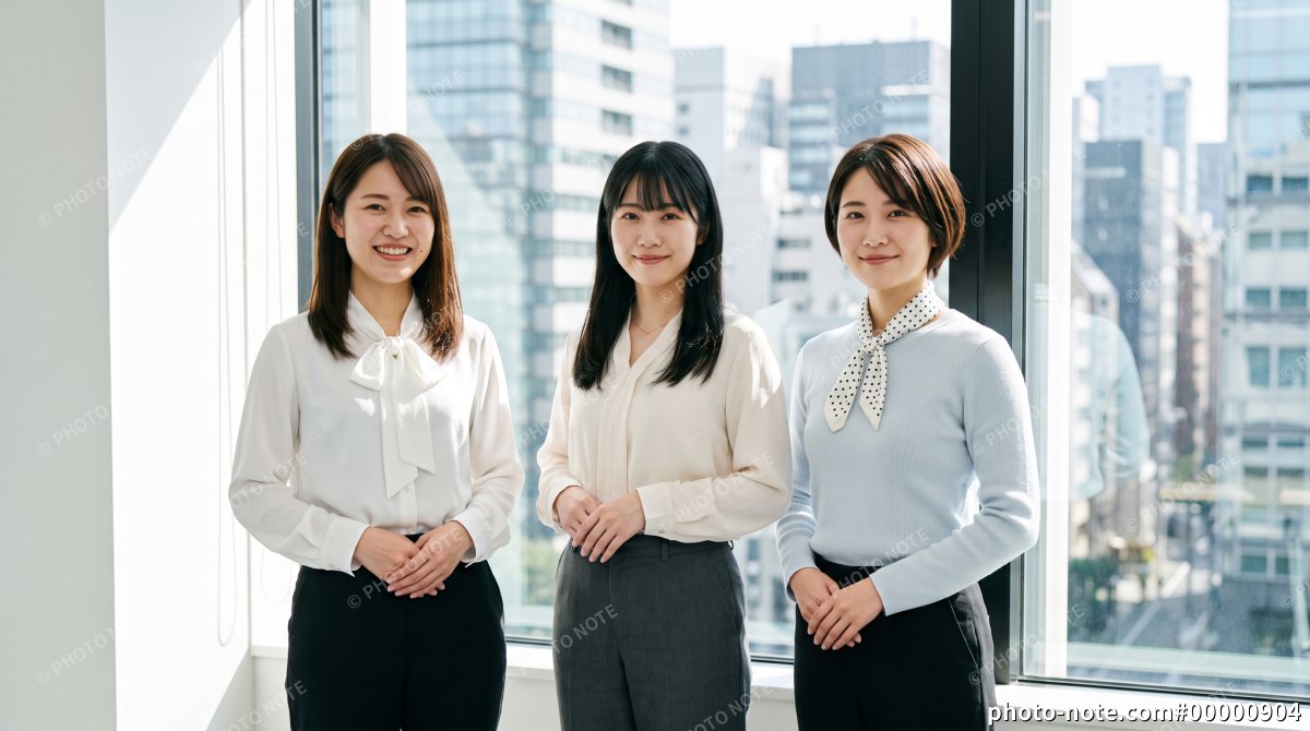 オフィスビルの窓際で並んで立つ一般事務の女性社員3人