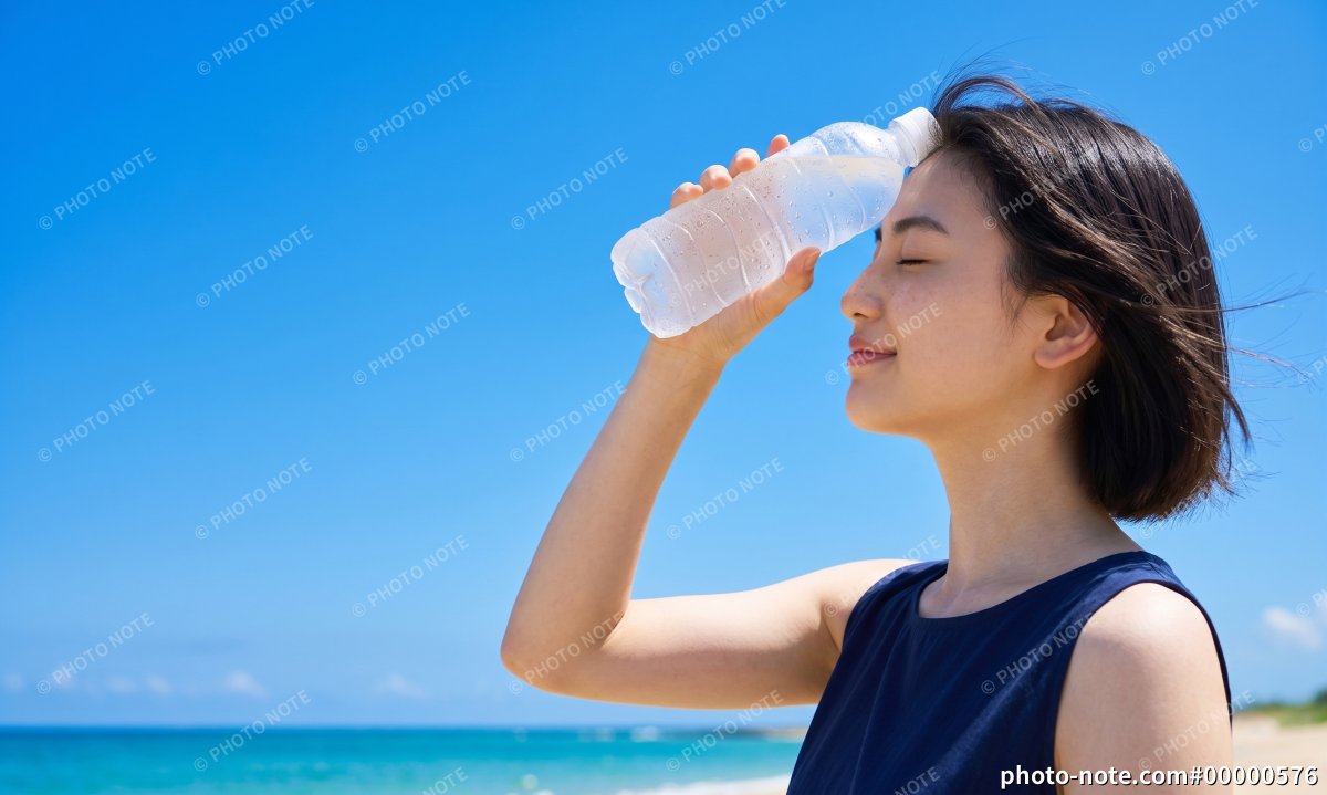 青空と海を背景に冷たいペットボトルで涼む女性