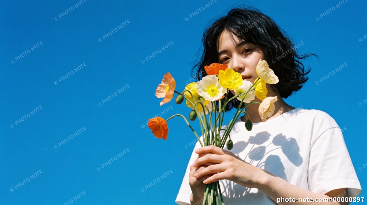 青空を背景にカラフルなポピーの花束を胸元に持つ若い女性