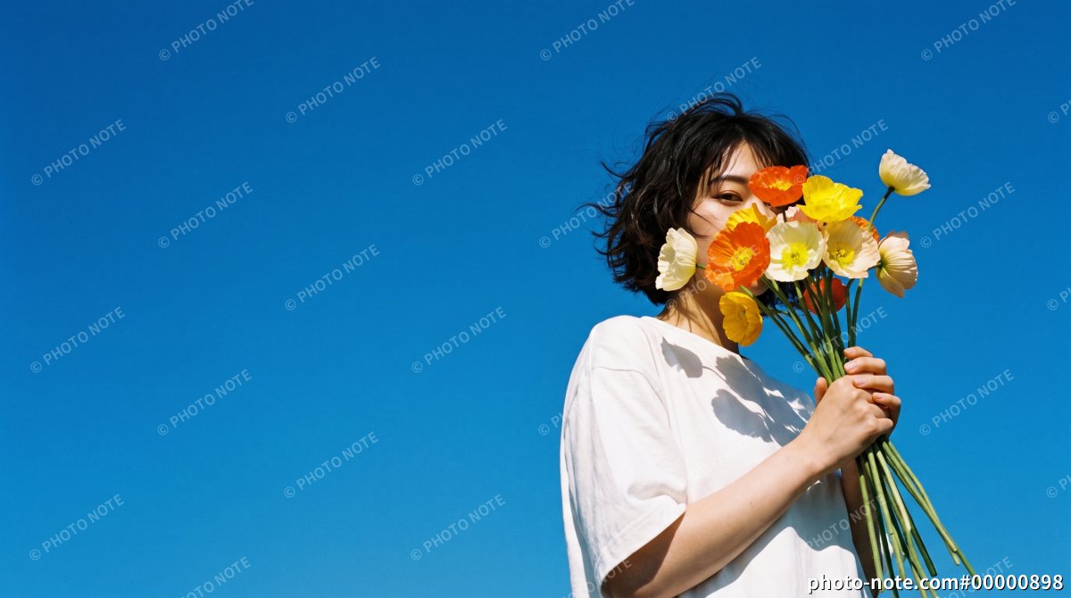 青空の下でポピーの花束を両手で顔の前に掲げる若い女性
