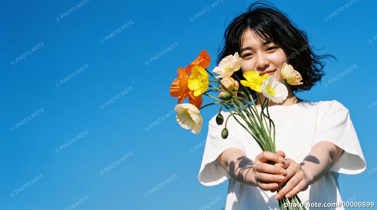 快晴の青空の下でカラフルなポピーの花束を前に差し出す若い女性