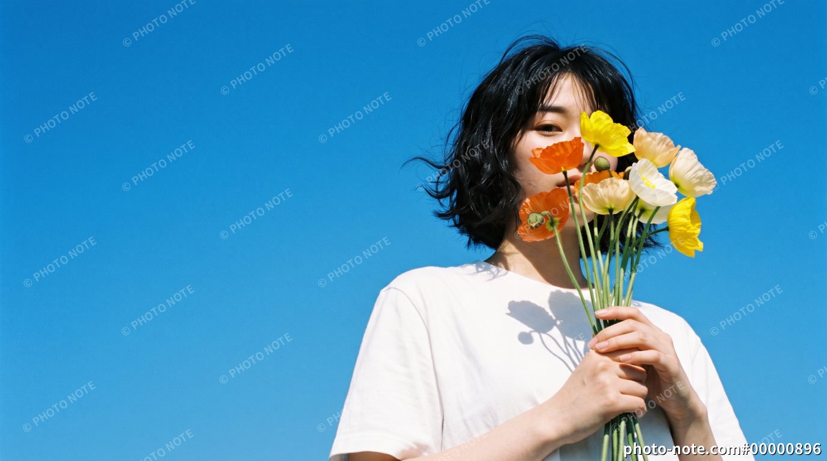 快晴の青空の下でポピーの花束を手に持ち口元を隠す若い女性