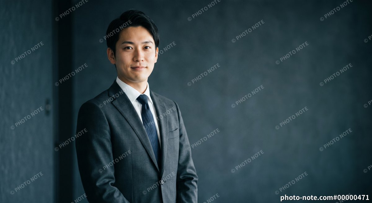 ダーク背景の前に立つ、自信に満ちた若手ビジネスマン