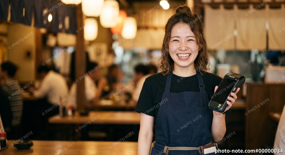 飲食店で決済端末を持つ笑顔の若い女性 、キャッシュレス決済